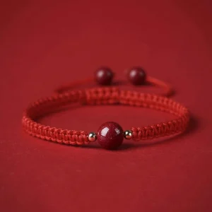 Cinnabar red string bracelet with braided rope and central bead on red fabric background