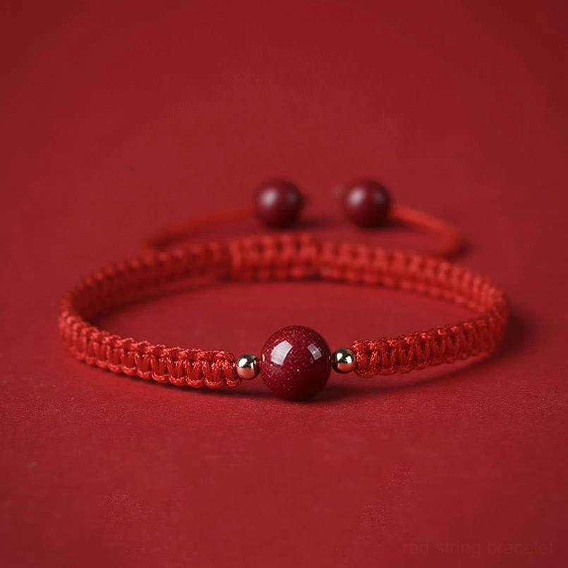 Cinnabar red string bracelet with braided rope and central bead on red fabric background