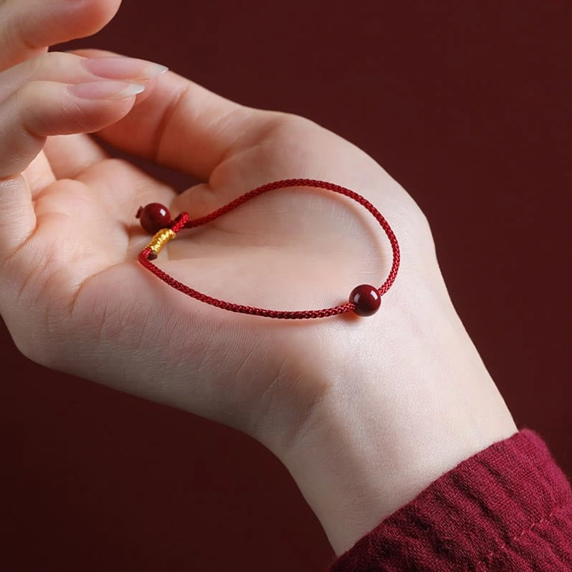 Handmade cinnabar red string bracelet held in palm showing dual beads and gold clasp