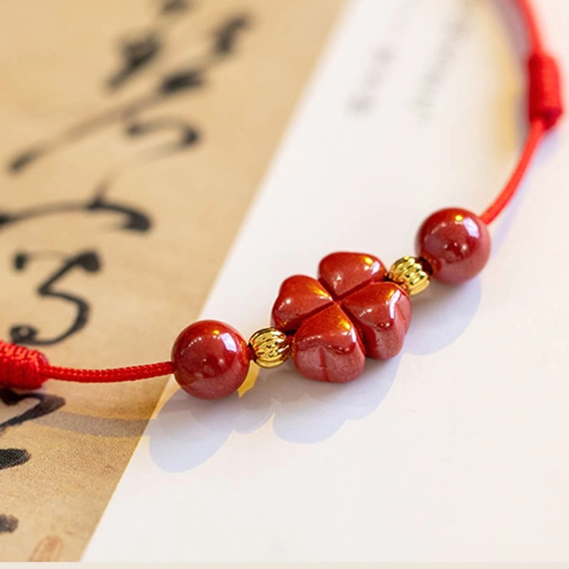 Side close-up of red woven rope cinnabar bracelet with four-leaf clover charm and gold spacers