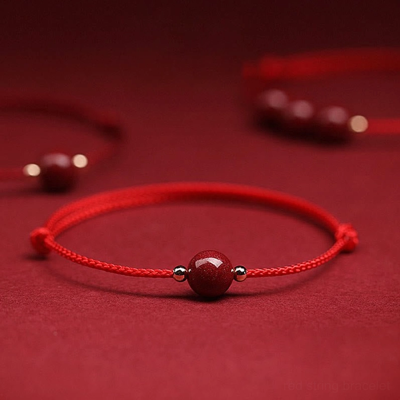 Single cinnabar bead red string bracelet flat lay with metal spacers on red fabric background