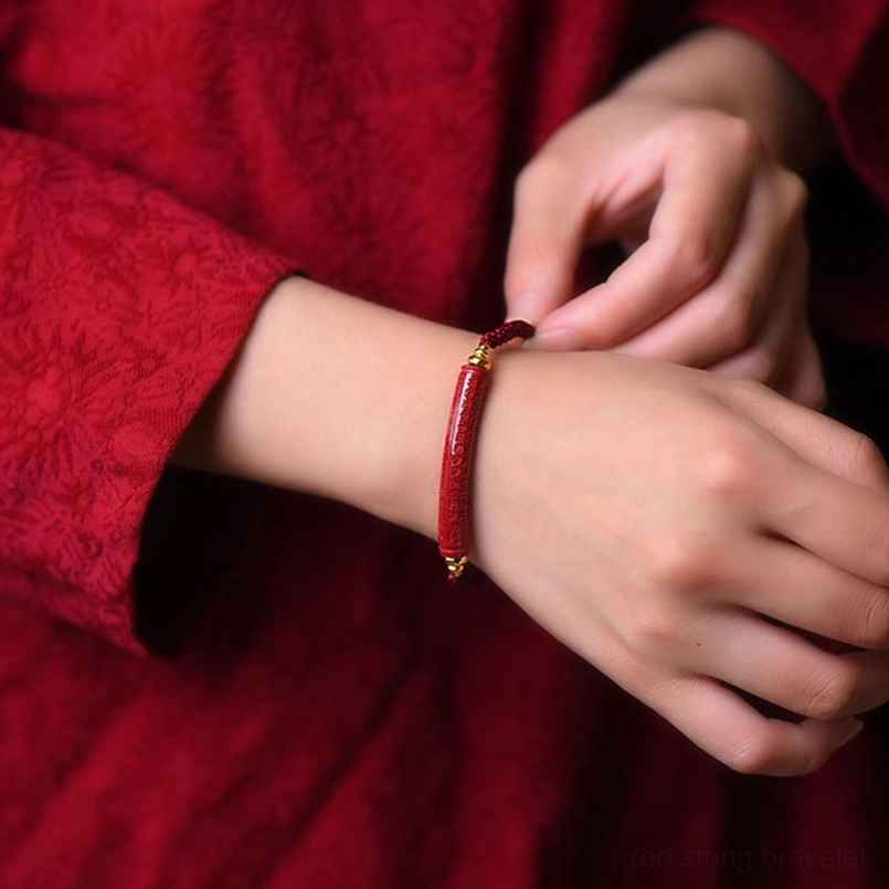 Adjustable cinnabar red string bracelet worn on human wrist closeup shot