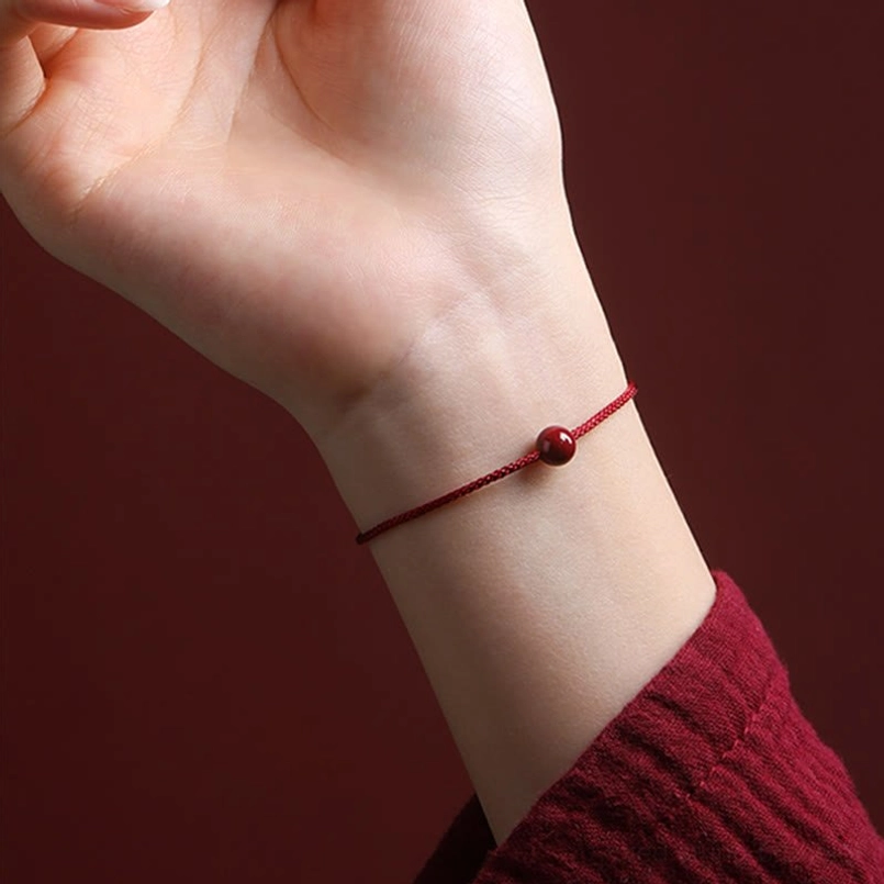 Worn cinnabar red string bracelet close-up showing thin braided cord detail