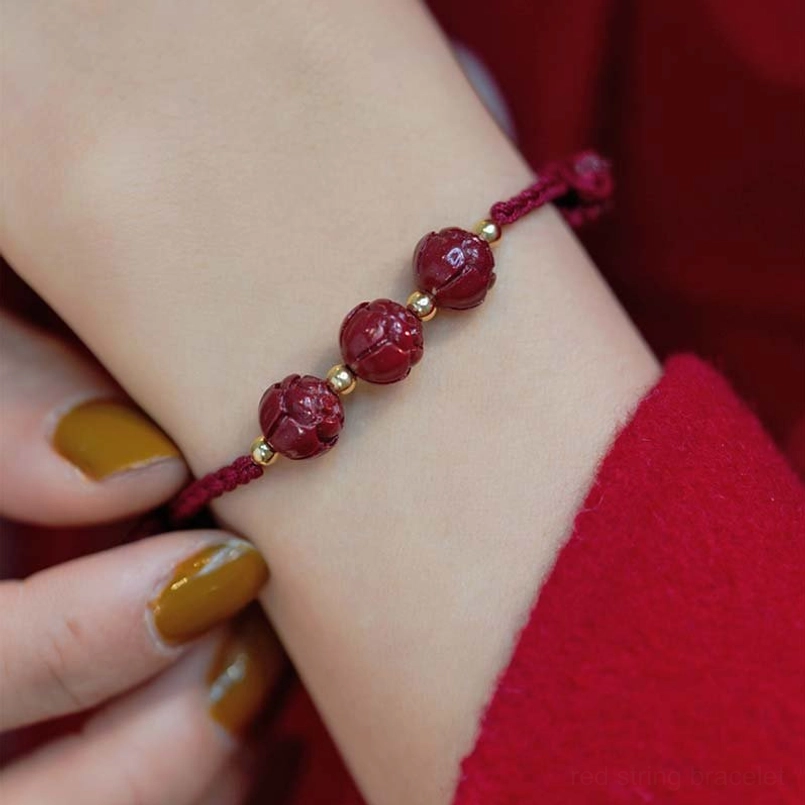 Single cinnabar bead red string bracelet on wrist with carved details and gold accents