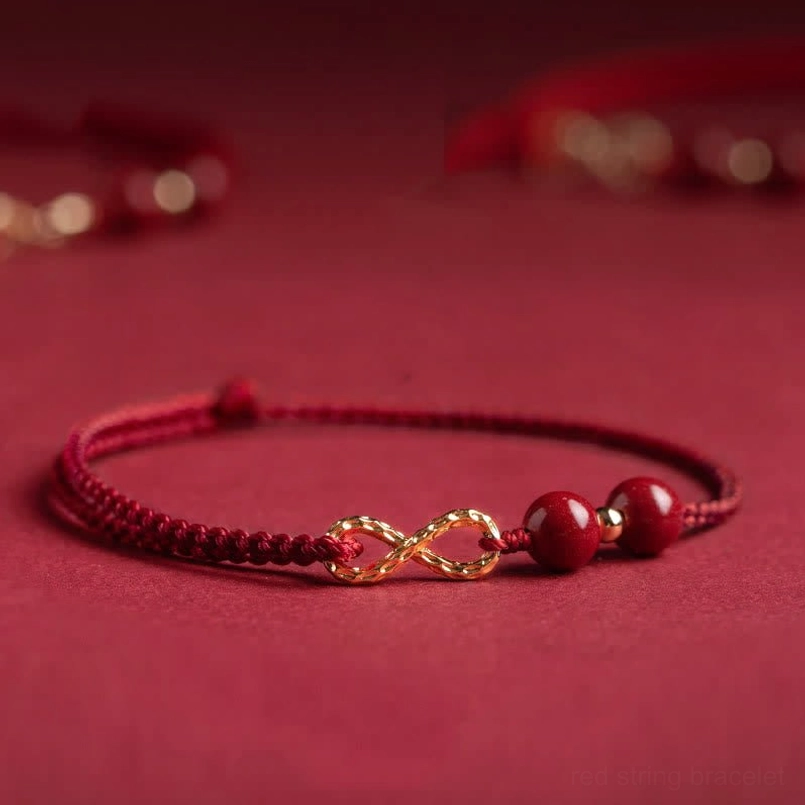 Dark red cinnabar beads with gold infinity symbol on premium braided red string, flat lay top-down view
