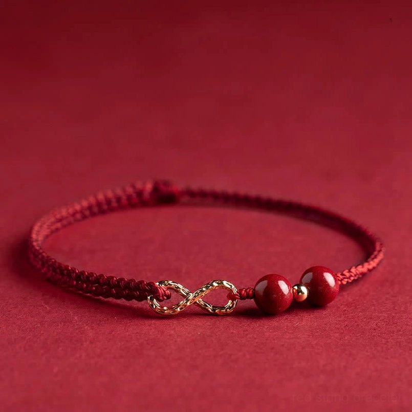 Cinnabar red string bracelet with gold infinity symbol and beads, side flat lay view on wine red background