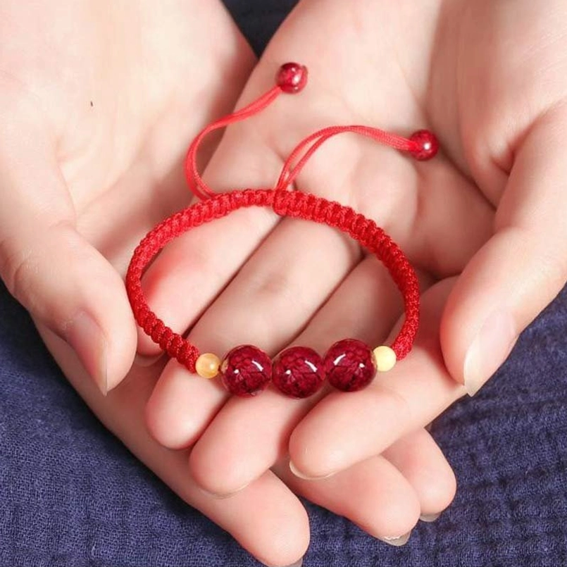 Red cinnabar and light yellow bead bracelet held in hand, braided rope design with adjustable tail