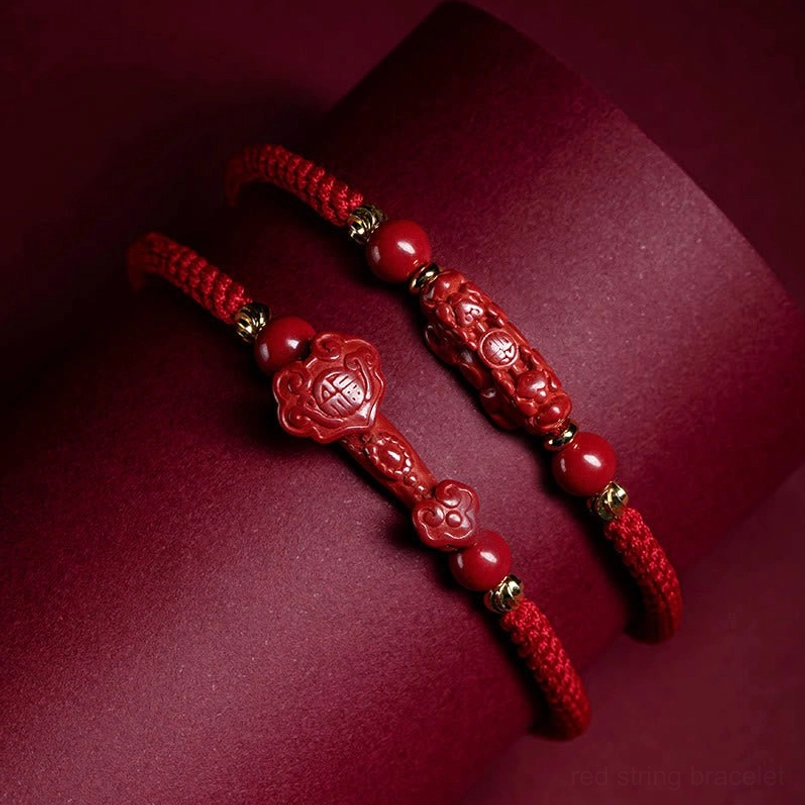 Two cinnabar red braided bracelets with Ruyi and PiXiu charms on dark red cushion