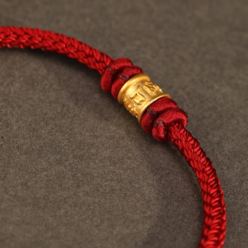 Close up side view of engraved 999 gold Om Mani Padme Hum bead on red bracelet