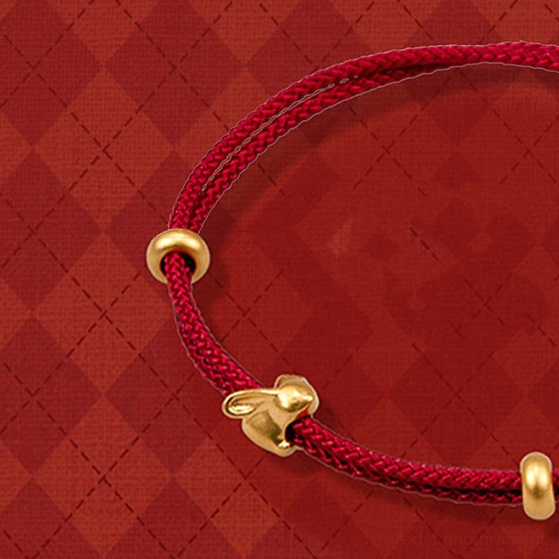 close up of gold rabbit charm red braided bracelet on red diamond backdrop