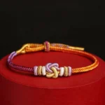 Colorful heart knot protection string bracelet with orange wine red purple and gold threads on display stand