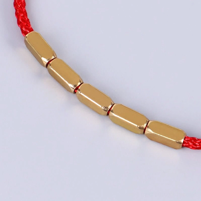 Close-up detail of copper beads on red braided string, side angle view