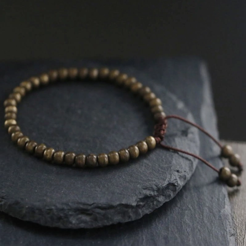 Copper brass beaded red string bracelet placed on stacked dark stone coasters