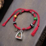 Copper Buddha Amitabha red string bracelet with braided cord and beads on wooden surface