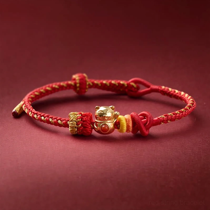 Side overhead view of copper cat charm red string luck bracelet on dark maroon background