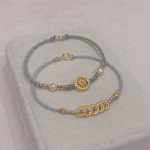 Blue copper coin fortune tree pearl bracelet set displayed on light gray tray, flat lay perspective showing gold coin charms and pearl accent with grey-blue braided rope