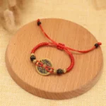 Single copper coin red string bracelet with black beads on wood surface, handmade Tibetan style