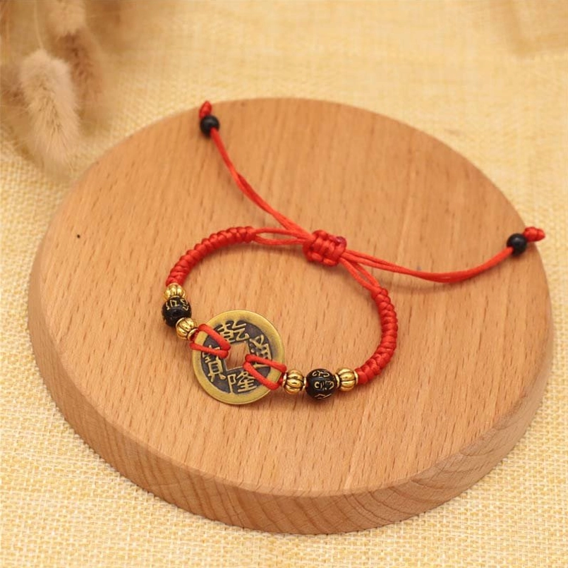 Single copper coin red string bracelet with black beads on wood surface, handmade Tibetan style