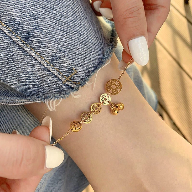 Hand adjusting copper coins bell anklet showing delicate coin and bell design