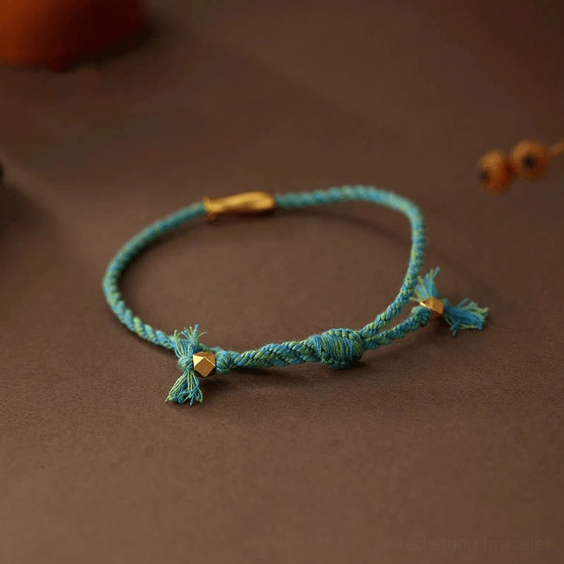 Blue-green braided luck bracelet with gold koi charm and tasseled rope ends side view