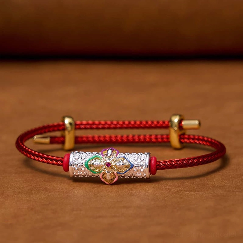 Top-down view of red string luck bracelet with central enamel flower bead on brown background, displaying full bracelet design