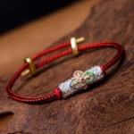 Copper luck red string bracelet with colorful flower charm on wooden surface, showing braided red cord and gold adjustable clasp