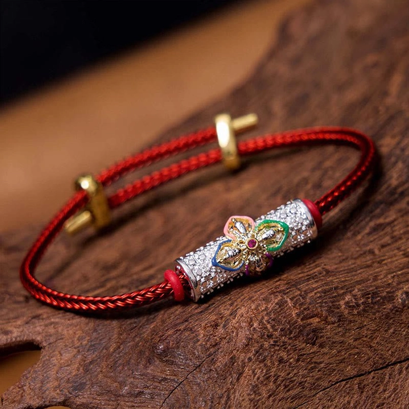 Copper luck red string bracelet with colorful flower charm on wooden surface, showing braided red cord and gold adjustable clasp