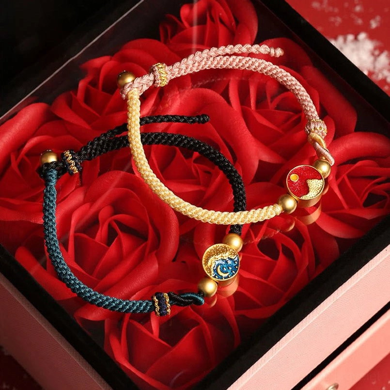 Matching couple red string bracelets with beige navy ropes and enamel charms displayed in romantic gift box with roses