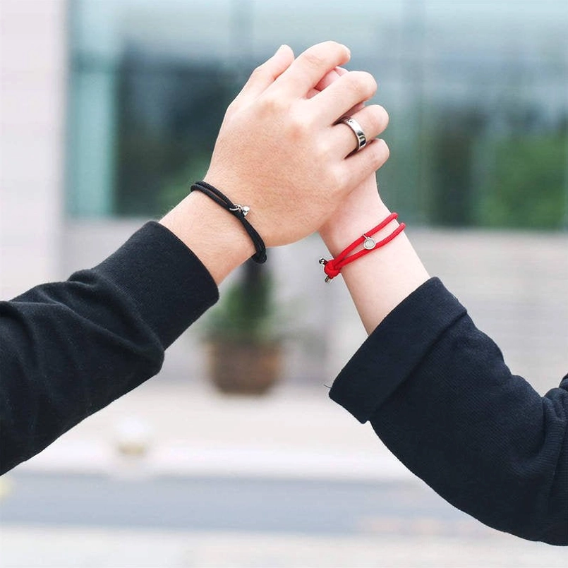 Couple holding hands wearing red and black magnetic string bracelets outdoors