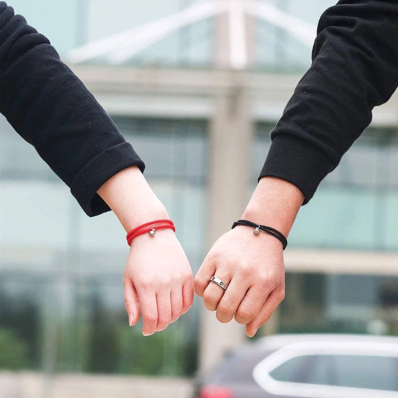 Couple linked hands wearing matching red black woven string bracelets, outdoor lifestyle