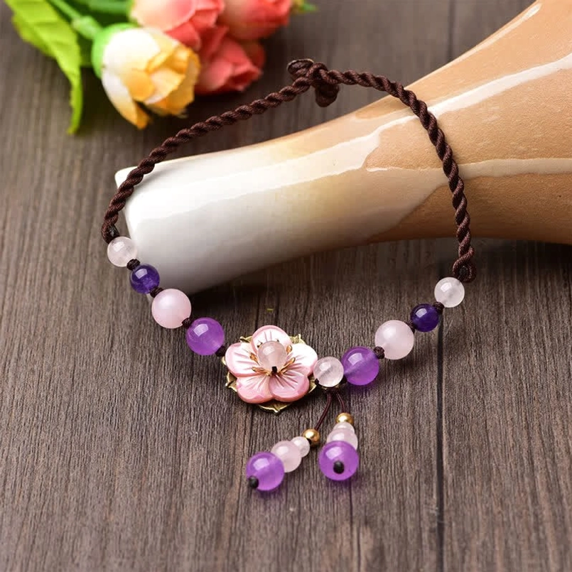 Top-down view of braided cord crystal anklet with central floral bead and dangling tassel accent