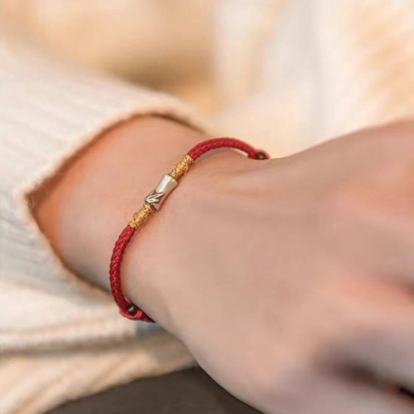 Slim red string bracelet with silver accents on cream knit background