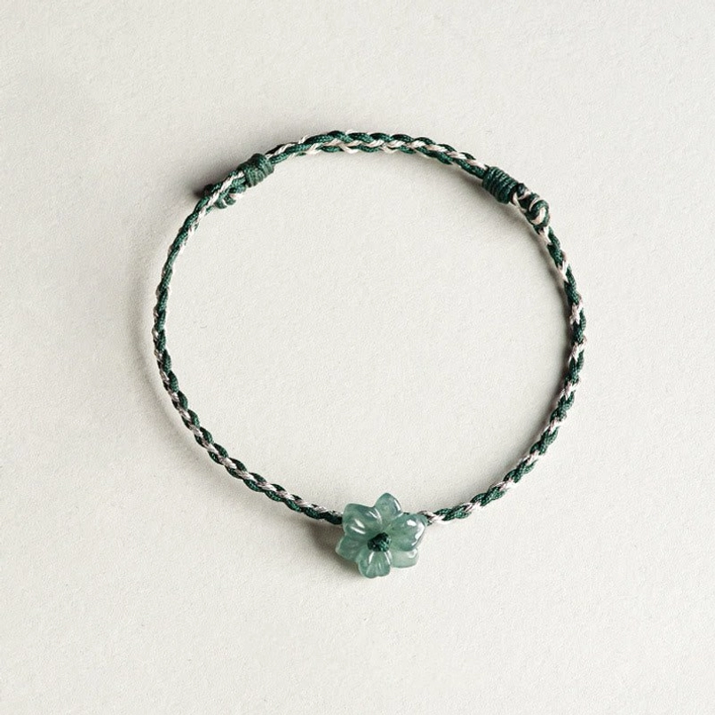 Top down view of dark green braided jade orchid bracelet on light gray desktop