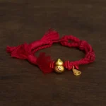 Dark red braided red string bracelet with gold gourd coin charm on dark wooden table