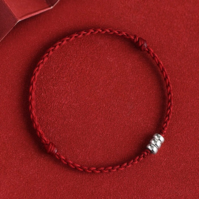 Dark red woven bracelet with sterling silver beads positioned on red fabric background