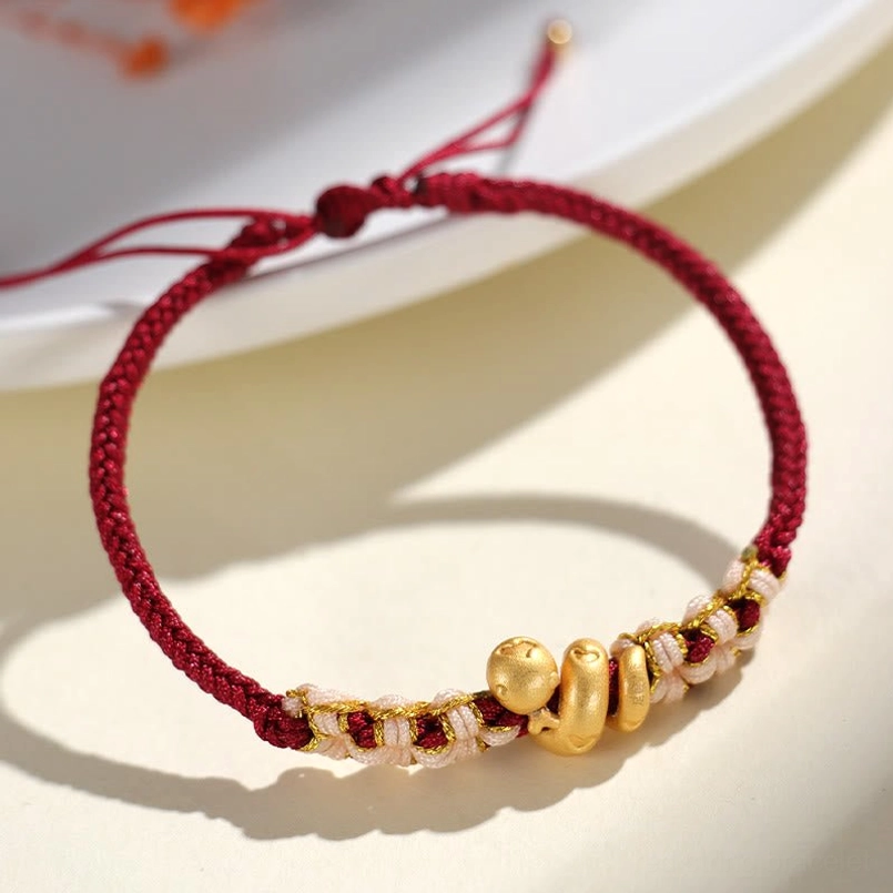 Side view of dark red string snake charm bracelet on white ceramic plate
