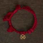 Dark red string bracelet with hollow copper lotus pendant flat lay on wooden table