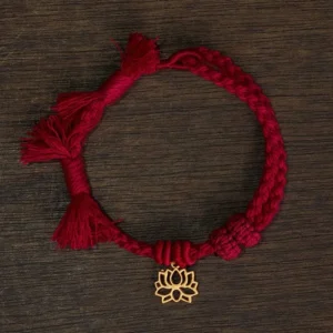 Dark red string bracelet with hollow copper lotus pendant flat lay on wooden table