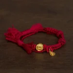 Dark Red Rope Lucky Bracelet with Gold Coin and Gourd Charms on Dark Wooden Table