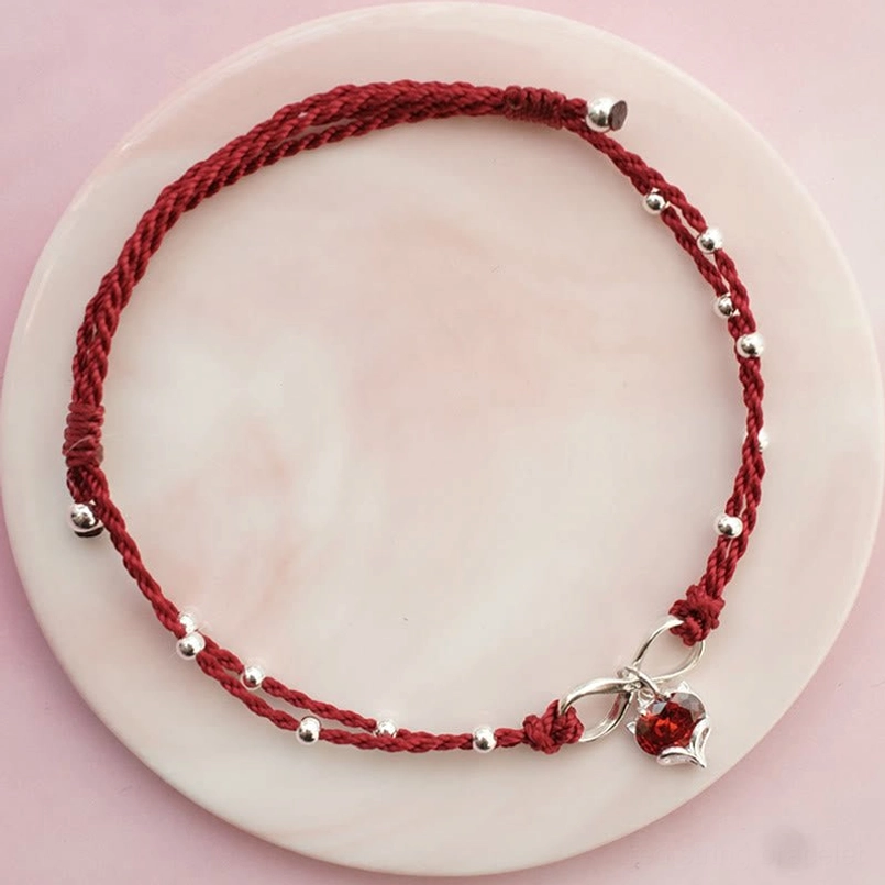 Dark red braided string anklet with unique silver bead layout and heart pendant on pink plate, dark red variant