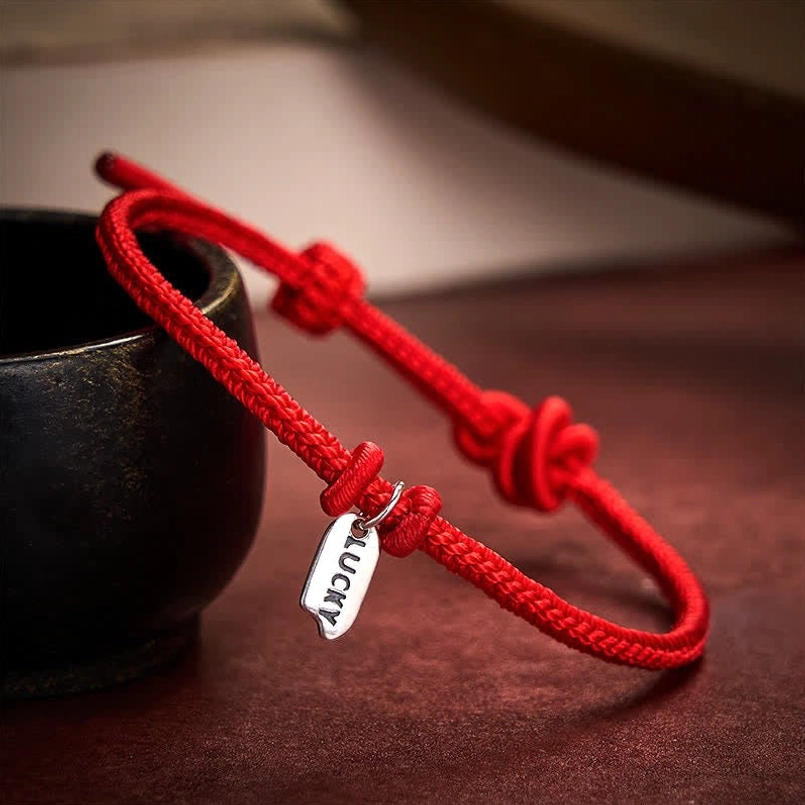 Dark red handmade lucky charm bracelet with LUCKY charm on wooden desk lifestyle shot