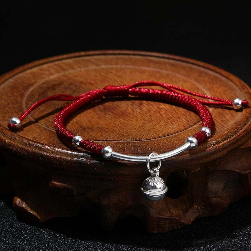 Dark red string protection bracelet with silver bell on wooden base