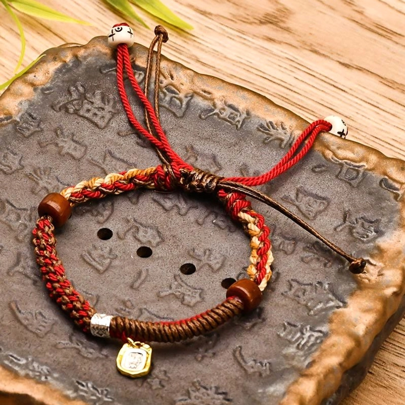 Dark red Tibetan braided Zakiram goddess of wealth bracelet on carved vintage stone tray