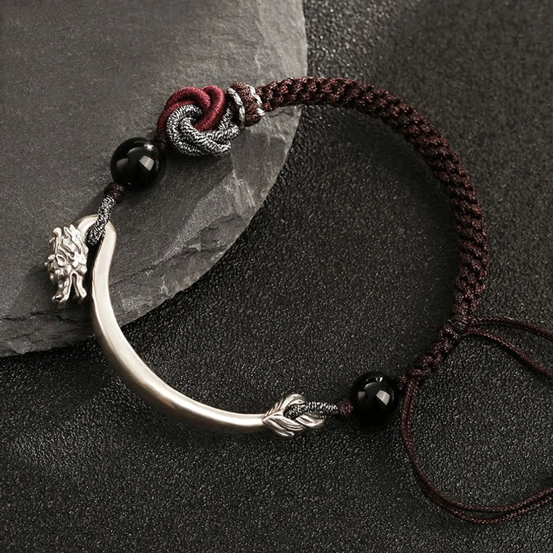 Sterling silver dragon bracelet with knotted cord ends and charm accent on dark desktop surface