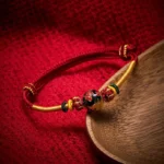 Dragon bead red string braided bracelet with copper details on wooden surface