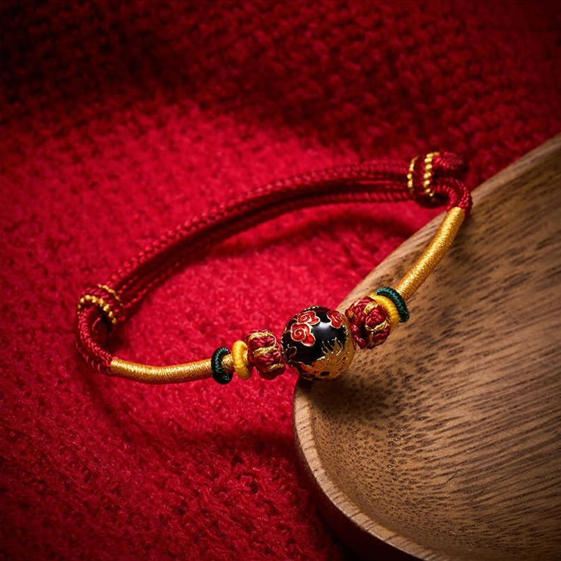 Dragon bead red string braided bracelet with copper details on wooden surface