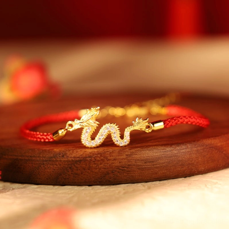 Dragon Year Red String Bracelet with gold dragon charm on wooden base