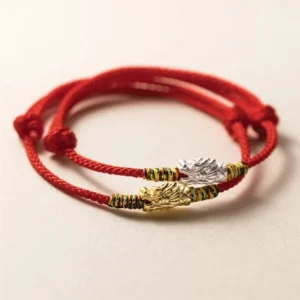 Dragon red string bracelet in silver and gold with braided cord and adjustable knots on plain background