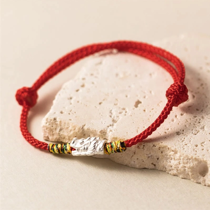 Silver dragon charm red string bracelet displayed on stone surface with adjustable side knots