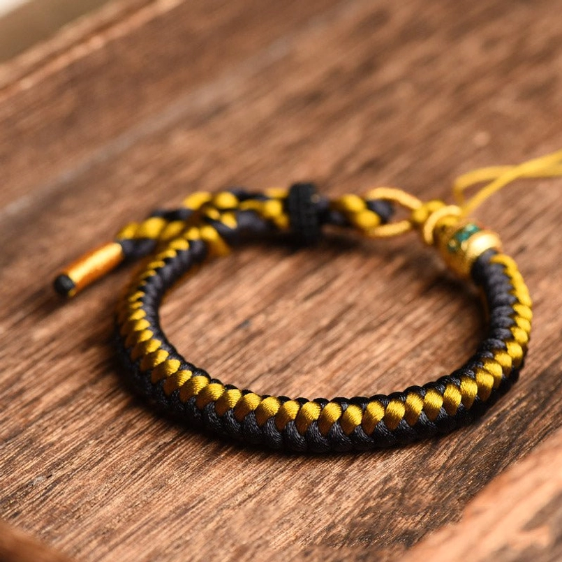 Woven black gold dragon scale bracelet flat lay showing twisted rope texture and adjustable closure